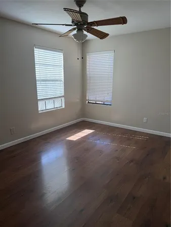 an empty room with wooden floor fan and windows