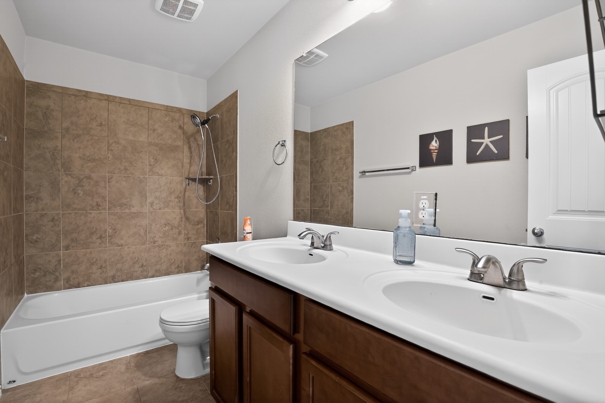 16816 Ruggio Road Pflugerville, TX 78660 - Photo 21 of 30 Modern bathroom featuring dual sinks, a large mirror, and tiled bath/shower combination.