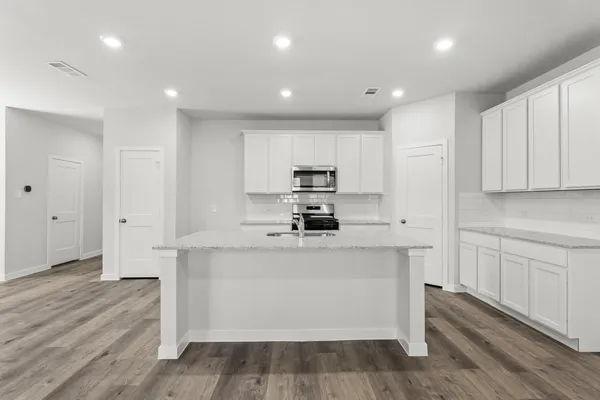 a large kitchen with stainless steel appliances granite countertop a stove a refrigerator a sink and white cabinets with wooden floor