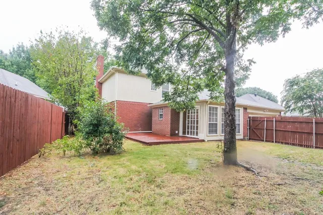 a backyard of a house with plants and large tree