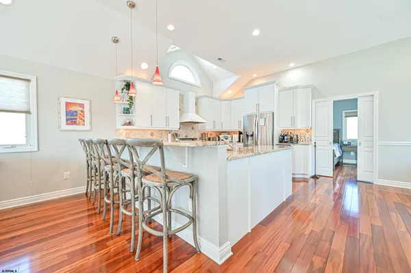 a kitchen with stainless steel appliances granite countertop a refrigerator a sink dishwasher a dining table and chairs with wooden floor