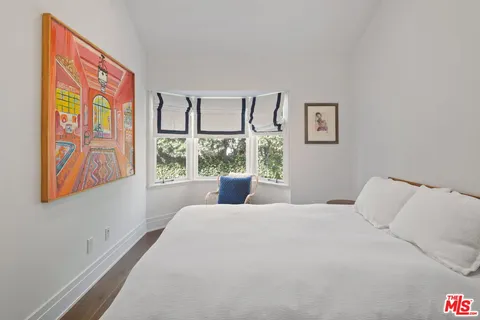 a bedroom with a bed painting on wall and a large window