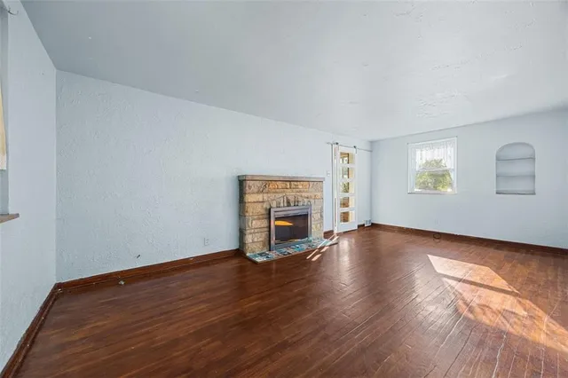 an empty room with wooden floor fireplace and windows