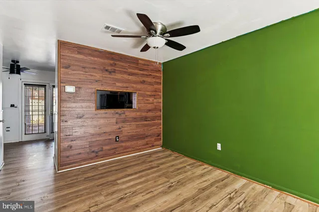a view of an empty room with wooden floor and a ceiling fan