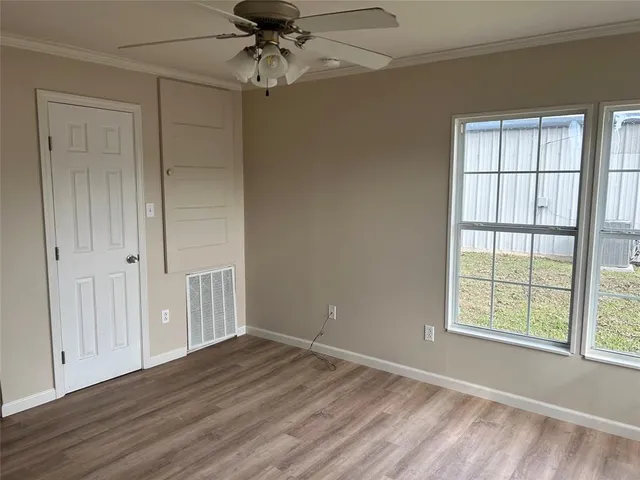 an empty room with wooden floor chandelier fan and windows
