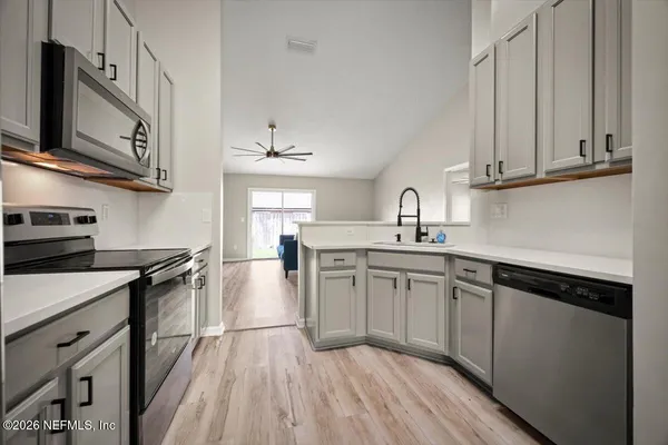 a kitchen with stainless steel appliances granite countertop a sink dishwasher stove and white cabinets with wooden floor