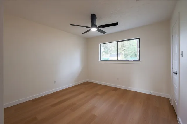 an empty room with wooden floor ceiling fan and windows