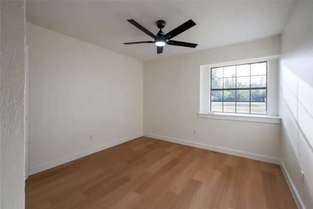 an empty room with ceiling fan and windows