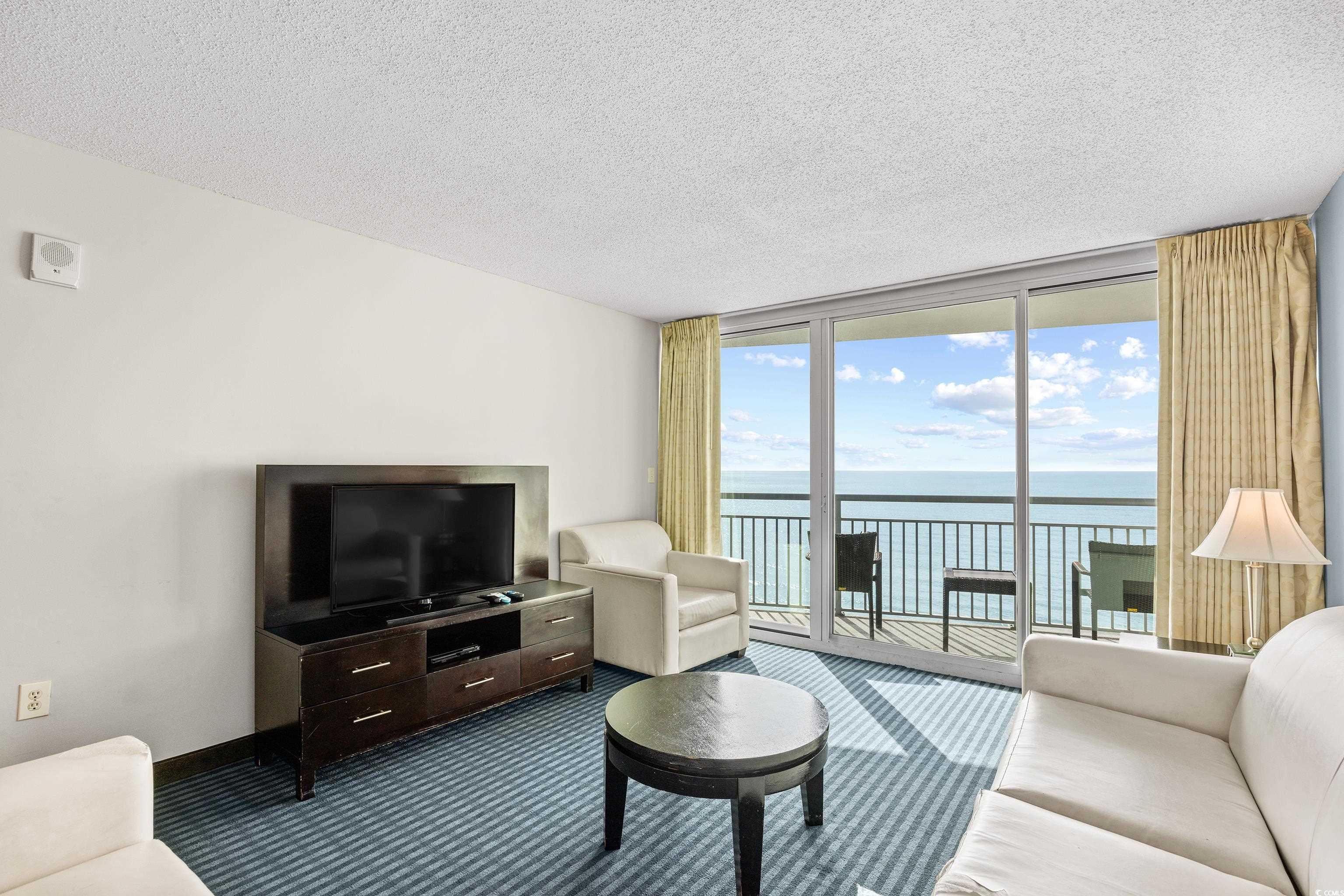 107 Ocean Boulevard, Unit 1402 Myrtle Beach, SC 29577 - Photo 8 of 38 Living room with a textured ceiling, a wall of windows, and dark carpet