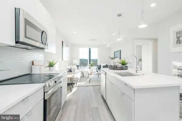 a large white kitchen with a stove a sink a refrigerator and white cabinets with wooden floor