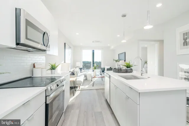 a large white kitchen with a stove a sink a refrigerator and white cabinets with wooden floor