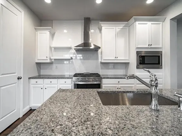 a kitchen with stainless steel appliances granite countertop a sink a stove a microwave and a white cabinets