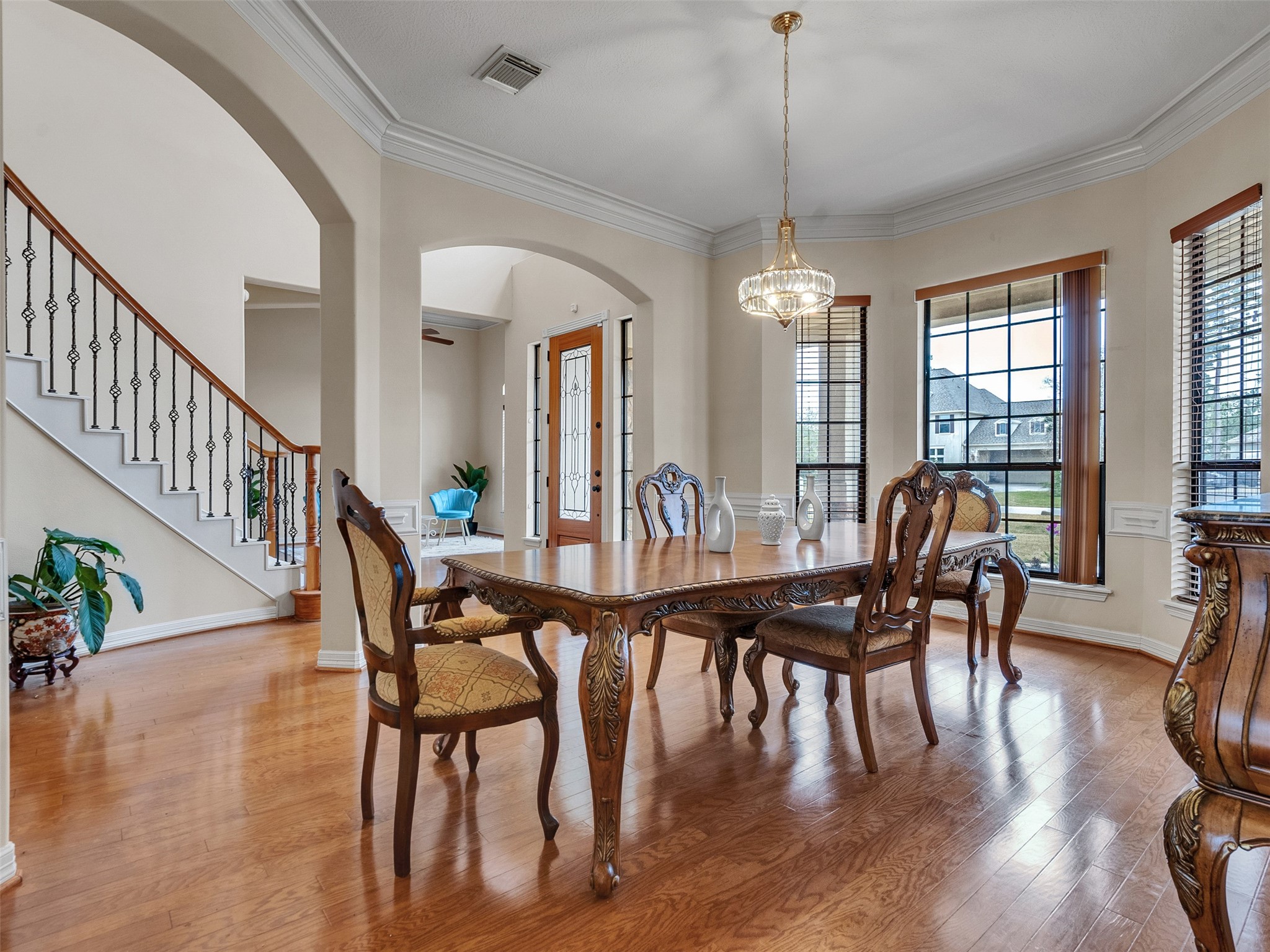 6914 Sandwedge Point Court Spring, TX 77389 - Photo 14 of 50 This elegant dining area features hardwood floors, a classic chandelier, and large windows offering natural light. The room showcases ornate wood furniture and leads to a staircase with decorative iron railings, creating a sophisticated ambiance.