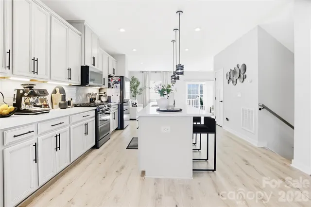 a kitchen with stainless steel appliances kitchen island granite countertop a stove a sink and white cabinets with wooden floor