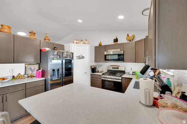 1284 North 900 West Clinton, UT 84015 - Photo 11 of 22 Kitchen with backsplash, stainless steel appliances, vaulted ceiling, a peninsula, and light stone counters