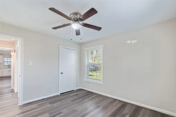 an empty room with wooden floor chandelier fan and windows