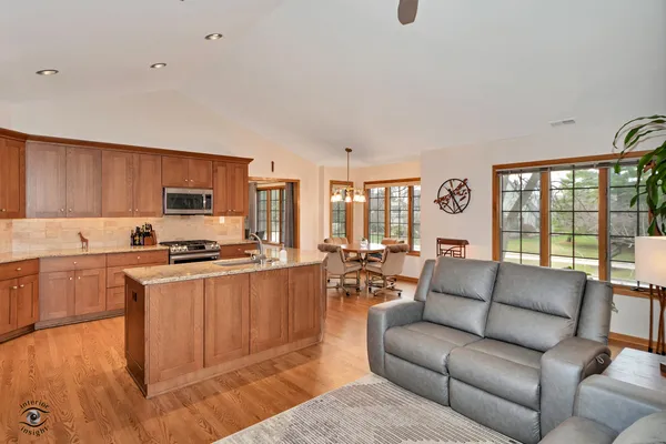 a large living room with stainless steel appliances granite countertop a couch a stove a flat screen tv and a window