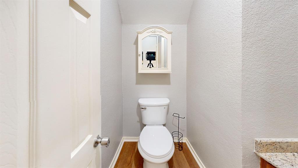 7913 Rice Drive Rowlett, TX 75088 - Photo 19 of 25 Neutral-toned powder room featuring wood-finish flooring, a white toilet, and a decorative mirrored medicine cabinet