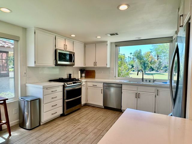 a kitchen with stainless steel appliances granite countertop a stove top oven a sink dishwasher a microwave oven and a refrigerator with wooden floor