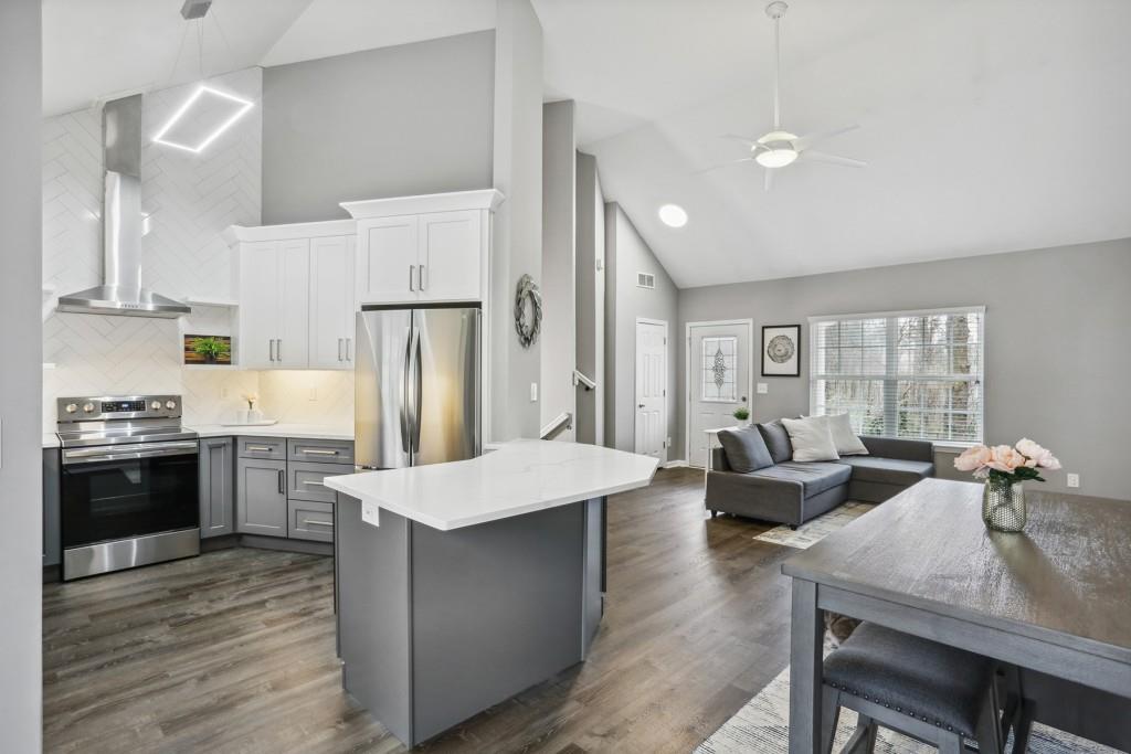 a large kitchen with stainless steel appliances kitchen island granite countertop a refrigerator a stove a sink a dining table and chairs with wooden floor