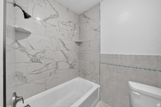 220 East Greenwood Avenue Midvale, UT 84047 - Photo 18 of 46 Bathtub and shower combination with floor-to-ceiling marbled tile surround, featuring a built-in shower niche and corner shelf