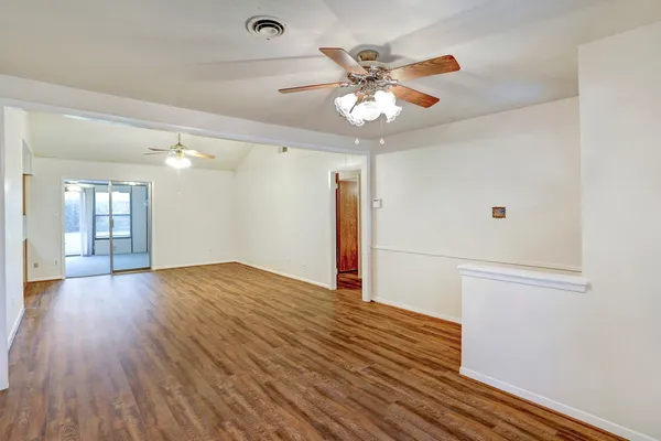 an empty room with wooden floor fan and windows