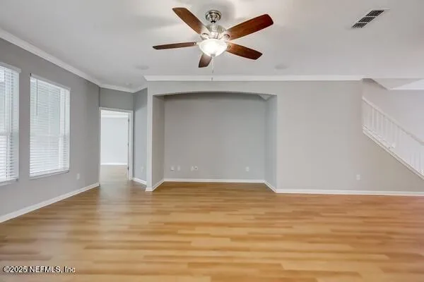 a view of an empty room with wooden floor and a ceiling fan