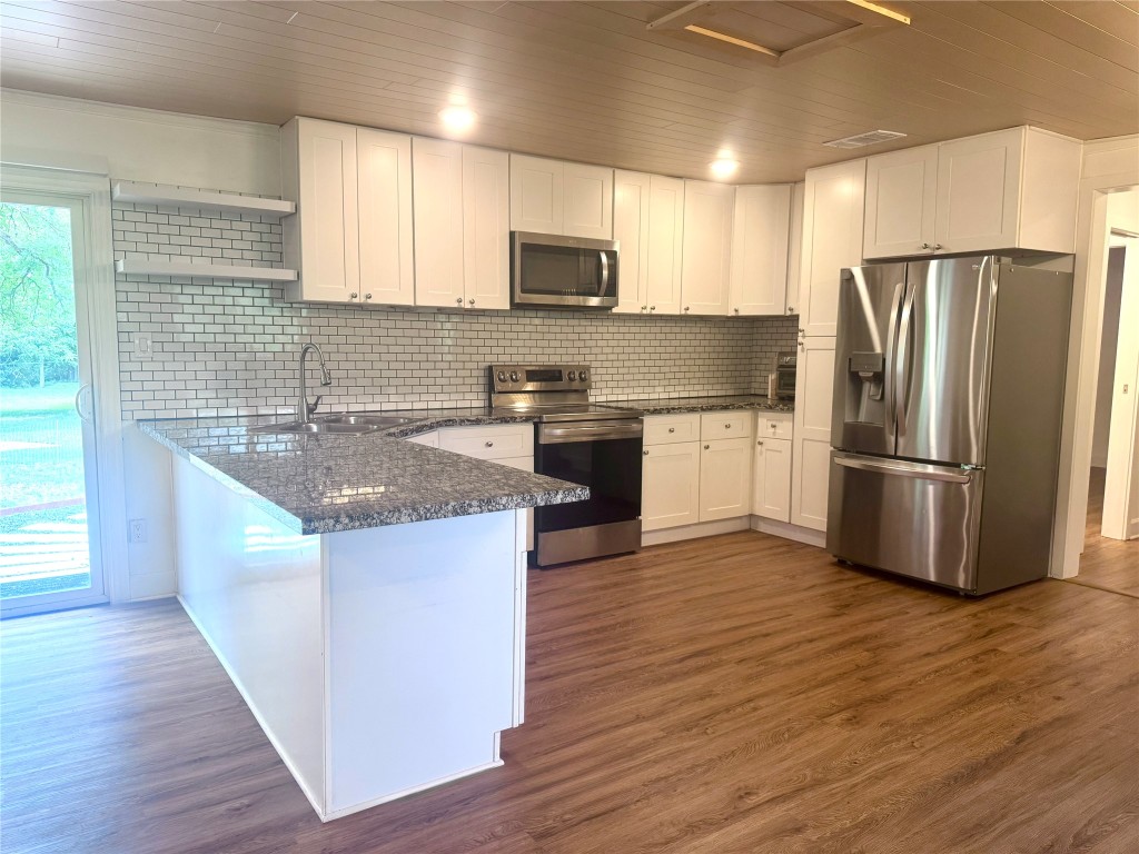 6011 Nuckols Crossing Road Austin, TX 78744 - Photo 11 of 24 Kitchen featuring open shelves, appliances with stainless steel finishes, white cabinets, dark wood-style floors, and dark stone countertops