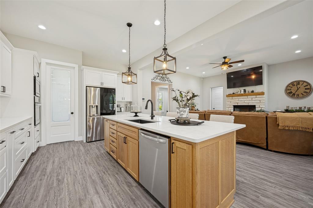 1105 Ranch Drive Bonham, TX 75418 - Photo 6 of 25 Expansive kitchen featuring a large island with sink, white granite countertops, built-in stainless steel appliances, and wood-finish flooring, decorative lighting and enough space for barstools around the island