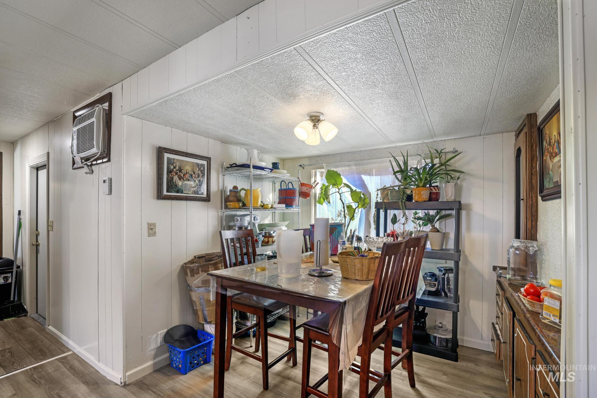 1625 Maple Street, Unit 20 Buhl, ID 83316 - Photo 6 of 17 Dining space featuring light wood-style floors, wooden walls, an AC wall unit, and a textured ceiling