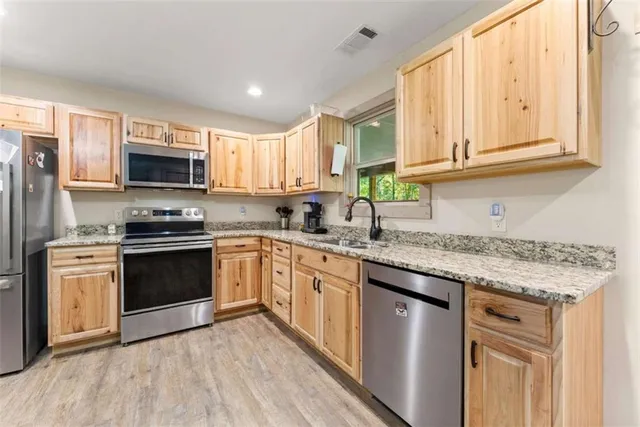 a kitchen with granite countertop a stove top oven a sink dishwasher and a refrigerator with wooden cabinets