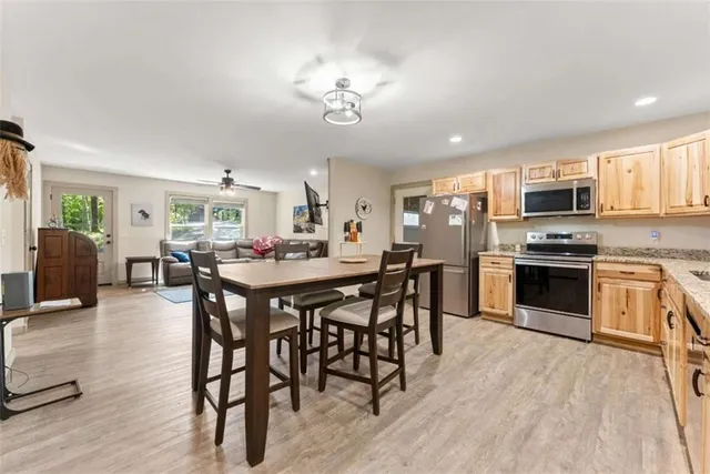 a kitchen with stainless steel appliances kitchen island granite countertop a stove top oven a sink a dining table and chairs with wooden floor