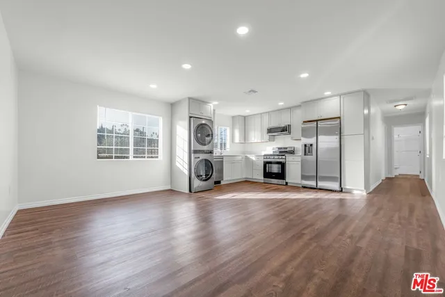 a view of a electric appliances in kitchen and empty room with wooden floor and windows