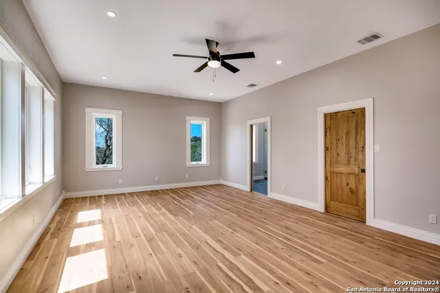 an empty room with wooden floor fan and windows