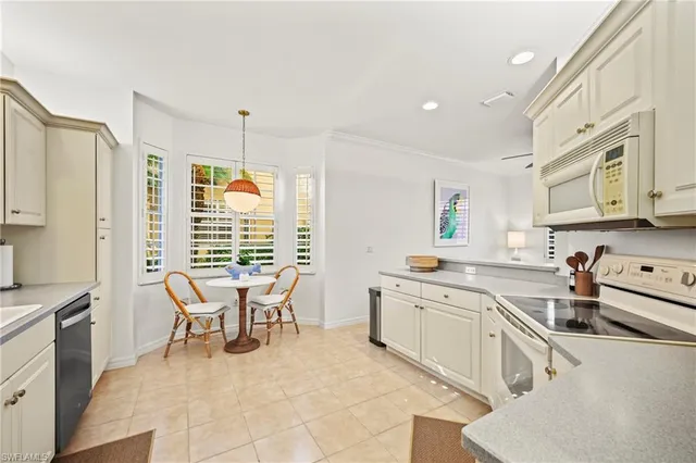 a large white kitchen with stainless steel appliances granite countertop a stove top oven a sink a dining table and chairs