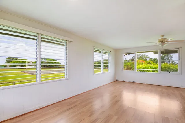 an empty room with wooden floor chandelier fan and windows