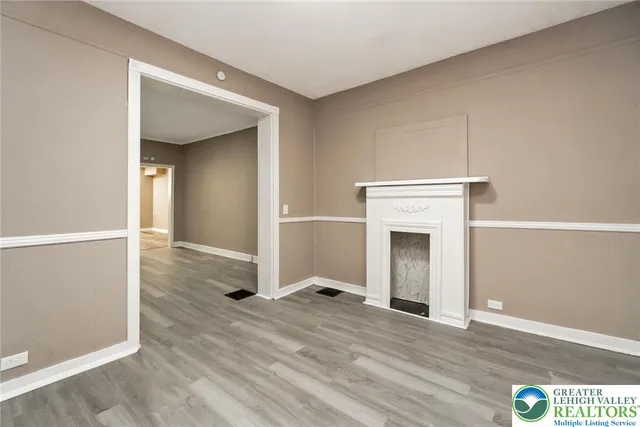 an empty room with wooden floor fireplace and windows