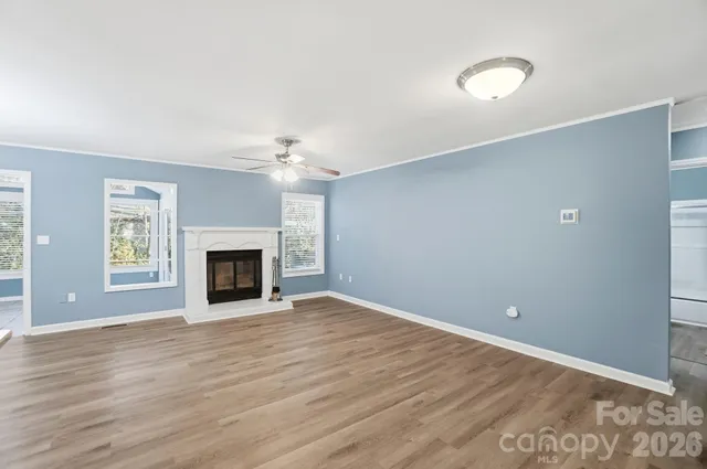 an empty room with wooden floor fireplace and windows