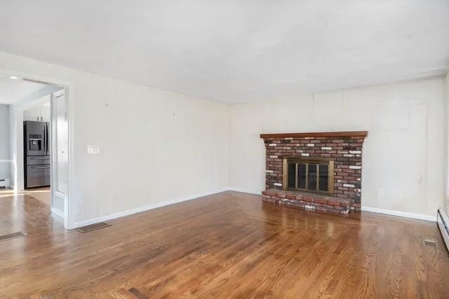 a view of an empty room with wooden floor fireplace and a window