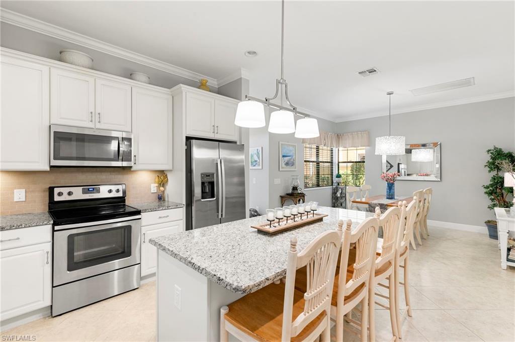 1350 Kendari Terrace Naples, FL 34113 - Photo 12 of 47 Kitchen featuring appliances with stainless steel finishes, a breakfast bar area, white cabinets, a center island, and ornamental molding