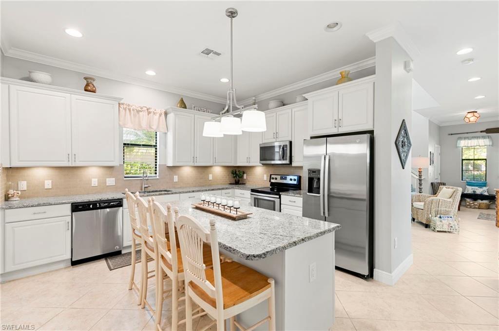 1350 Kendari Terrace Naples, FL 34113 - Photo 14 of 47 Kitchen featuring stainless steel appliances, a kitchen bar, light tile patterned flooring, light stone counters, and crown molding