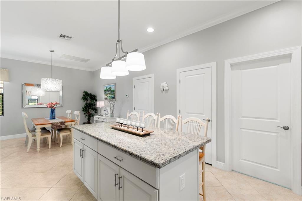 1350 Kendari Terrace Naples, FL 34113 - Photo 10 of 47 Kitchen with a breakfast bar area, light stone countertops, ornamental molding, decorative light fixtures, and light tile patterned floors