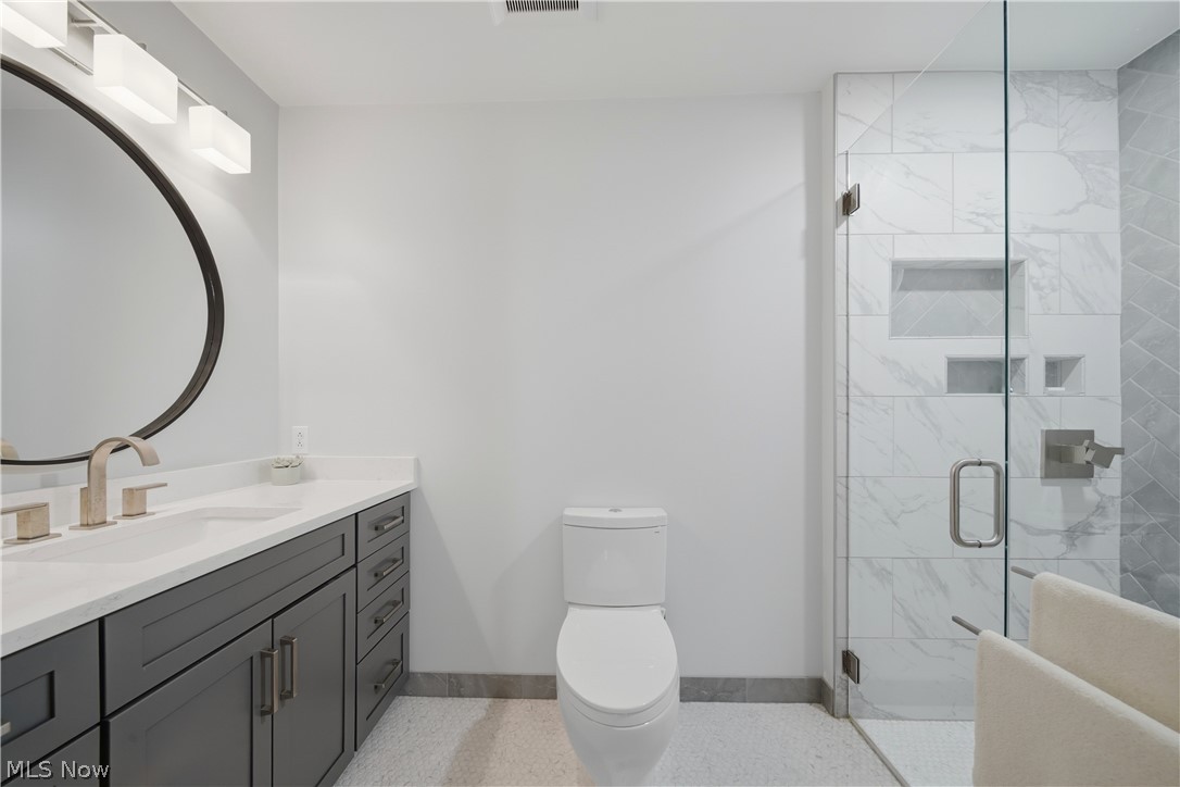 118 Manning Road Mogadore, OH 44260 - Photo 17 of 45 Modern bathroom featuring a frameless glass shower enclosure with white and grey tile, a contrasting vanity with a white countertop and rectangular undermount sink, a circular mirror, and brushed nickel fixtures