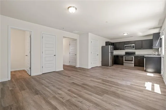 an empty room with wooden floor and kitchen view