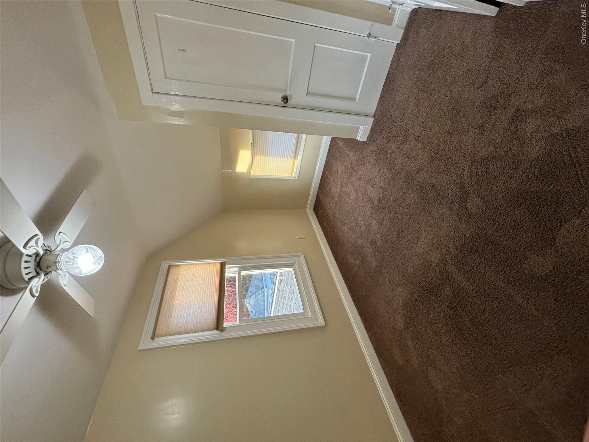 445 North Country Road St. James, NY 11780 - Photo 9 of 13 an empty room with a chandelier fan and windows