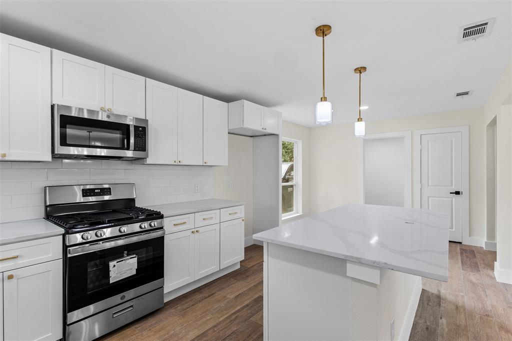 2816 Quail Ridge Drive Carrollton, TX 75006 - Photo 11 of 33 Kitchen featuring appliances with stainless steel finishes, white cabinets, backsplash, dark wood-type flooring, and a kitchen island