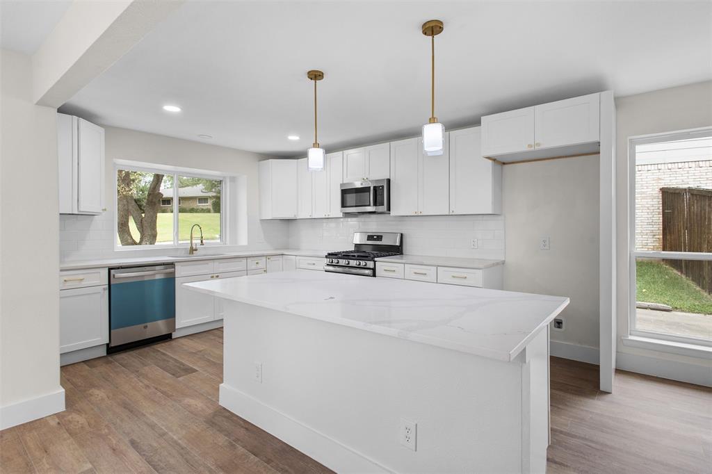 2816 Quail Ridge Drive Carrollton, TX 75006 - Photo 9 of 33 Kitchen with tasteful backsplash, a center island, appliances with stainless steel finishes, white cabinetry, and light wood-type flooring