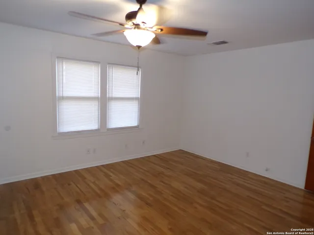 a view of empty room with wooden floor and fan