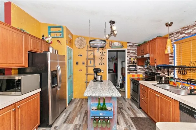 a kitchen with stainless steel appliances kitchen island granite countertop a refrigerator a stove top oven a sink dishwasher and wooden cabinets with wooden floor