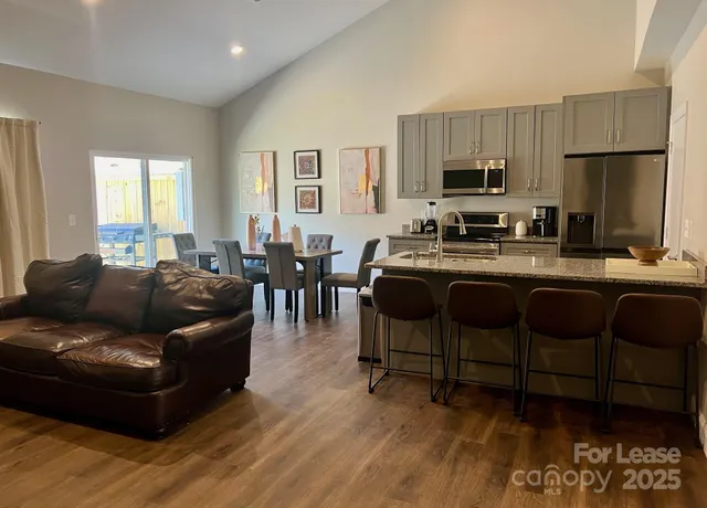 a living room with furniture a dining table wooden floor and a refrigerator